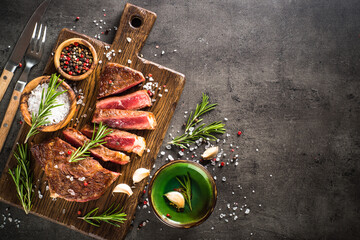 Grilled Beef steak at wooden cutting board with spices. Top view with copy space at black background.