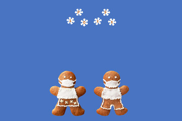 PF 2022 inscribed in snowflakes falling on gingerbread couple with protective face masks. Original New Year greeting card in coronavirus (COVID-19) time, isolated on blue background, copy space 