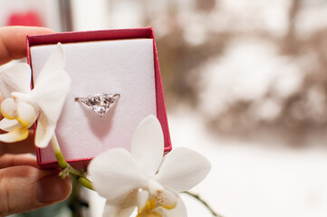 a ring with a large gemstone in a box next to orchid flowers with a blurred background