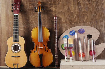 Attributes of the arts. Art palette, brushes, guitar, violin, bow, pipe on a wooden textured background. 