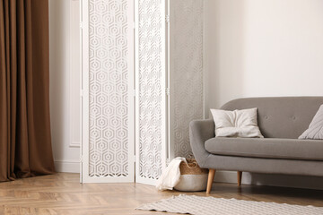 Stylish room with folding screen and sofa near white wall. Interior design