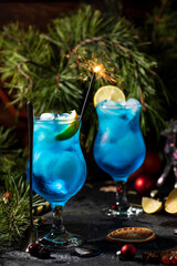 blue cocktail in a tall glass with ice and lemon slices on a wooden background