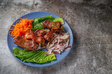 Serving a dish from the restaurant menu. Grilled beef and pork meat with grated carrots and herbs on a plate against a gray stone table, delicious kebab