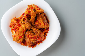 Ayam sambal balado or spicy fried chicken is Traditional food from Padang, West Sumatra. served on plate and isolated gray background.