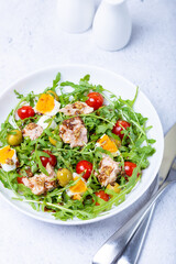Salad with tuna, arugula, tomatoes, olives and eggs in a white plate. A traditional dish. Close-up.
