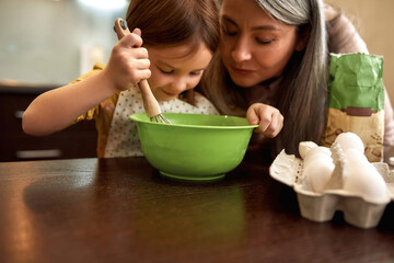 Obraz na płótnie Canvas Smiling girl mixing dough in bowl with grandmother