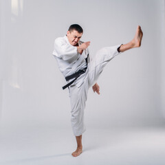 a young man, in a white kimano, shows the elements of karate in the studio on a white background