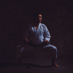 a young man, in a white kimano, shows the elements of karate in the studio on a black background