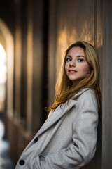 Fototapeta na wymiar smiling blonde teenage girl in coat leaning on the wall in the street