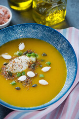 Close-up of pumpkin soup topped with soft cheese and pumpkin seeds in a blue bowl, vertical shot