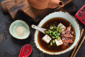 Bowl of miso soup with salmon, tofu and edamame on a brown stone background, high angle view,...