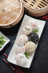White plate with onigiri or japanese stuffed rice balls, vertical shot on a dark brown stone background with a bamboo steamer