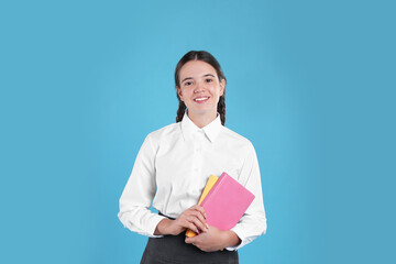 Obraz premium Teenage girl in school uniform with books on light blue background
