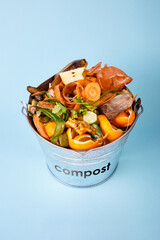 Sorted kitchen waste in compost-bucket on blue background. Compost-container top view. Sustainable lifestyle. Vegetable, fruit peels, scraps from food preparation collected in trash-can for recycling