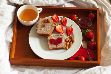 Romantic valentine's breakfast in bed:  tea, strawberry jam, whole wheat toast, jam heart, fresh strawberries and almonds , top view. Saint Valentines day greeting card