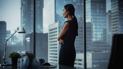 Fototapeta na wymiar Successful Businesswoman in Stylish Dress Looking out of the Window at Big City in Downtown Area. Confident Female CEO Working on Financial Projects. Manager at Work Planning Marketing Campaign.