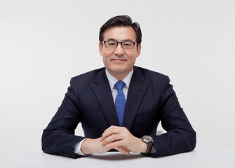 Middle-aged business man wearing a suit sitting at a desk and putting his hands together