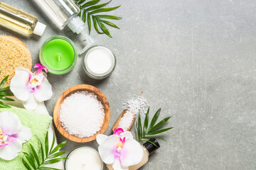 Fototapeta na wymiar Spa product composition with palm leaves, towel, bath salt and cosmetic at gray stone table. Healthcare concept. Flat lay image with copy space.