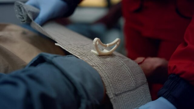 Unrecognizable paramedic in gloves wrapping man hand with elastic bandage