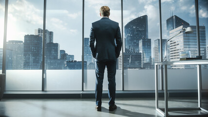 Fototapeta na wymiar Successful Young Businessman in a Perfect Tailored Suit Standing in His Modern Office Looking out of the Window on Big City with Skyscrapers. Successful Finance Manager Planning Project Strategy.
