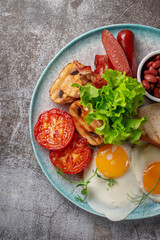 Serving a dish from the restaurant menu. Delicious and healthy breakfast with fried eggs, beans, sausages, grilled vegetables, tomatoes and mushrooms with salad on a plate against a gray stone table