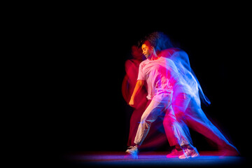 Sportive young girl in white costume dancing hip-hop dance isolated on dark background at dance hall in neon mixed light.