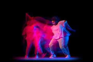 One young sportive girl in white costume dancing hip-hop dance isolated on dark background at dance hall in neon mixed light.