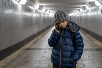 Portrait of a lonely confident boy in a hat and jacket talking on the phone in an underground...