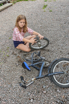 the child girl has damaged a bicycle wheel and is making repairs photo without processing