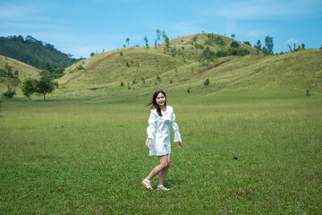 Obraz premium Beautiful Girl stand and acting in front of bald mountain or Phu Khao Ya with green grass field and blue sky. One of natural travel attraction in Ranong province, Thailand