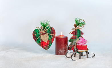 Christmas composition: a handmade heart, a toy sleigh with a gift and a candle on the background of a toy Christmas tree. Selective focus