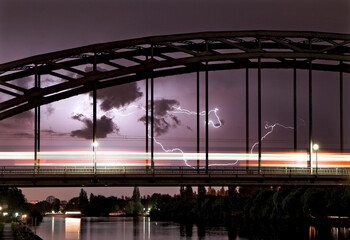 Ein über eine Bogenbrücke fahrender, durch Bewegungsunschärfe verwischter ICE bei Nacht und...