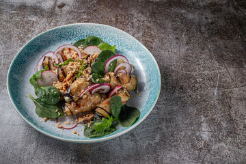 Serving a dish from a restaurant menu. Stuffed eggplants with onions, green spinach and walnuts on a plate against the background of a gray stone table
