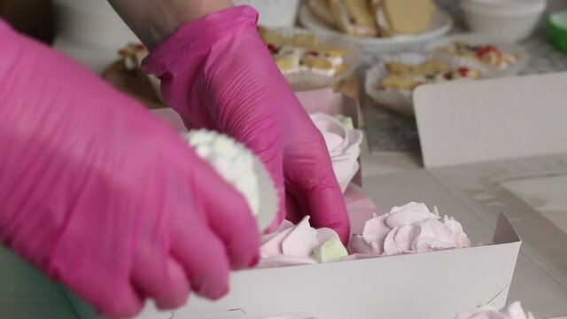 A woman is packing marshmallow roses in a box. Zephyro Sadwiches are on the table nearby. Close-up shot.