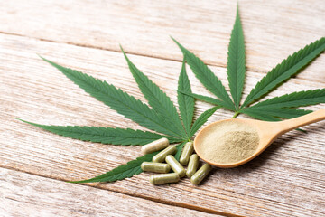 Cannabis leaf and cbd powder capsule pill isolated on wooden table background. 