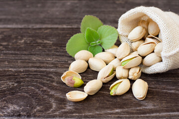 Pistachio nut in sack bag with mint green leaf on wooden table background.