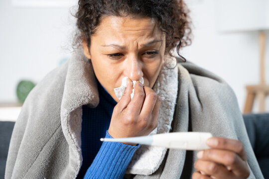 Black woman suffering cold and flu at home checking thermometer