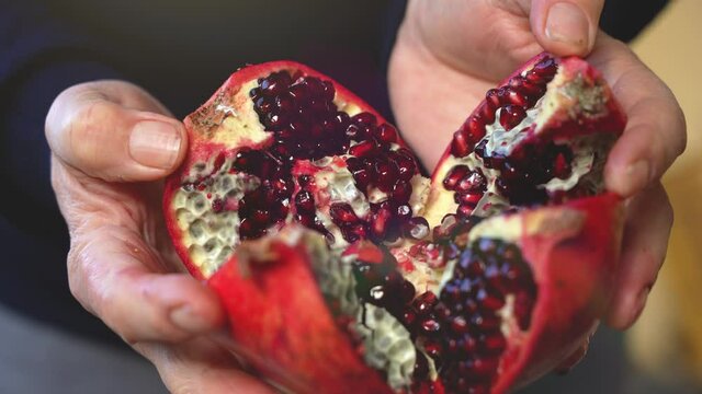 Closeup of a farmer woman opens an organic healthy vitaminic pomegranate divided into four parts under sunlight.