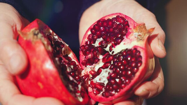 Closeup of a farmer woman opens and halves an organic healthy vitaminic pomegranate divided into two parts under sunlight.