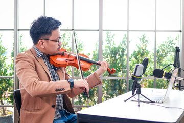 Asian male teacher teaching classical music lessons Play the violin for students to watch via online video calls on their laptops. Modern education concept, study online from home. © SUPERMAO