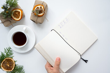Obraz na płótnie Canvas 2022 notepad female hand. The concept of goals and objectives. Planning for the next year. Top view of a creative desktop with gifts with a coffee mug. Happy New Year and Merry Christmas. Zero waste