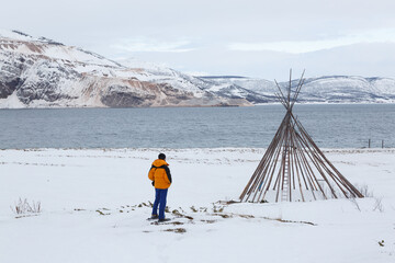 Man next to a Sami lavvo on the seashore