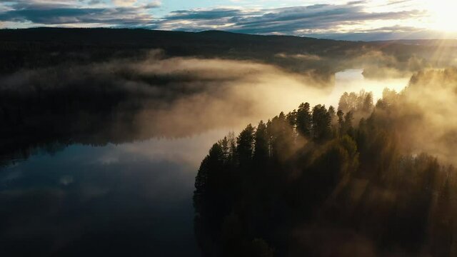 An aerial shot of a majestic sunset over a river running through a pine tree forest