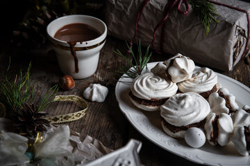 Meringue cookies with chocolate and almond cream and cup of hot chocolate, wrapped presents and natural winter decorations on old wooden table 