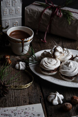 Meringue cookies with chocolate and almond cream and cup of hot chocolate, wrapped presents and natural winter decorations on old wooden table 