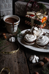 Meringue cookies with chocolate and almond cream and cup of hot chocolate, wrapped presents and natural winter decorations on old wooden table 