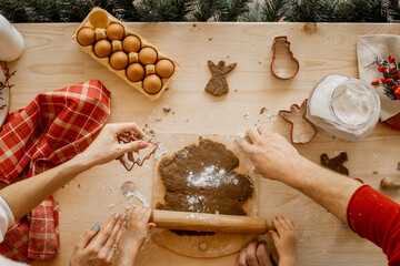 Fototapeta premium Close up of young family's hands prepare christmas cookies on a wooden table with a lot of cooking ingredients.