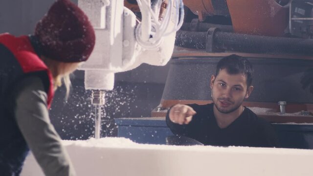 Man and woman talking and removing dust from block while drilling polymer with milling machine during work in modern workshop