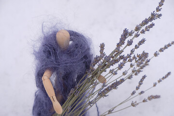 A wooden mannequin in a fur coat of purple mohair holds a dry lavender bouquet on a snow background.
