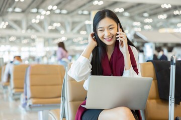 Confident beautiful young chinese woman sitting on bench at airport working or study on laptop and...